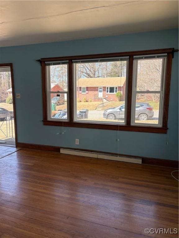 spare room with a baseboard heating unit, wood finished floors, and baseboards