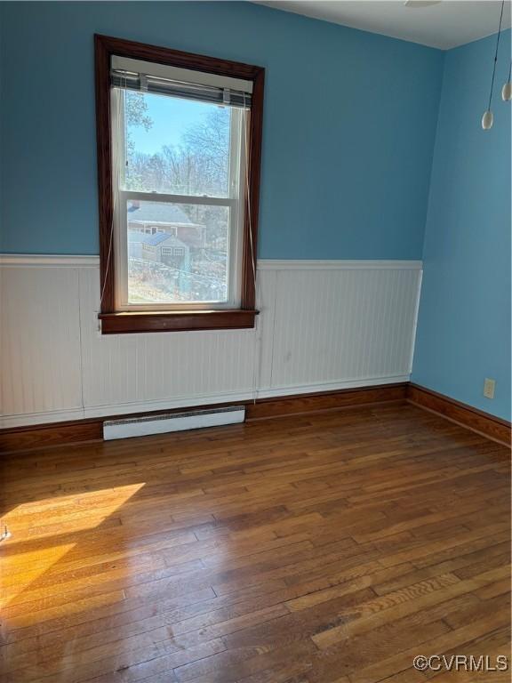 spare room featuring a baseboard heating unit, hardwood / wood-style floors, and a wainscoted wall