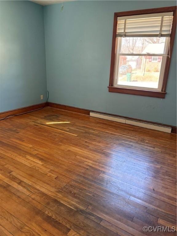 empty room featuring baseboards, hardwood / wood-style floors, and baseboard heating