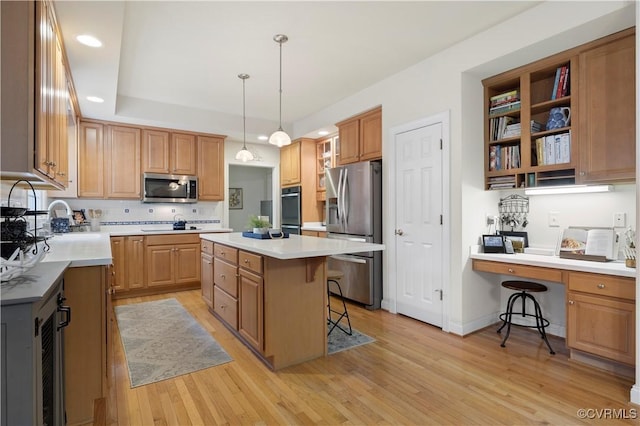 kitchen featuring light wood-style flooring, stainless steel appliances, a kitchen island, a kitchen breakfast bar, and built in study area