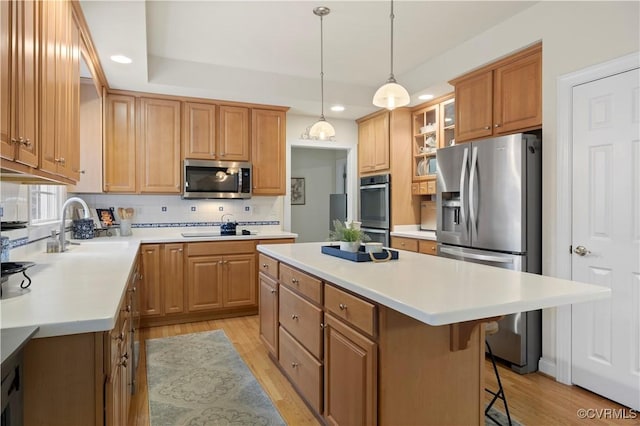 kitchen featuring a center island, light wood finished floors, decorative backsplash, appliances with stainless steel finishes, and a sink