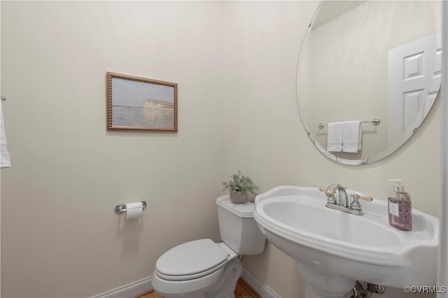 half bathroom with a sink, toilet, and baseboards