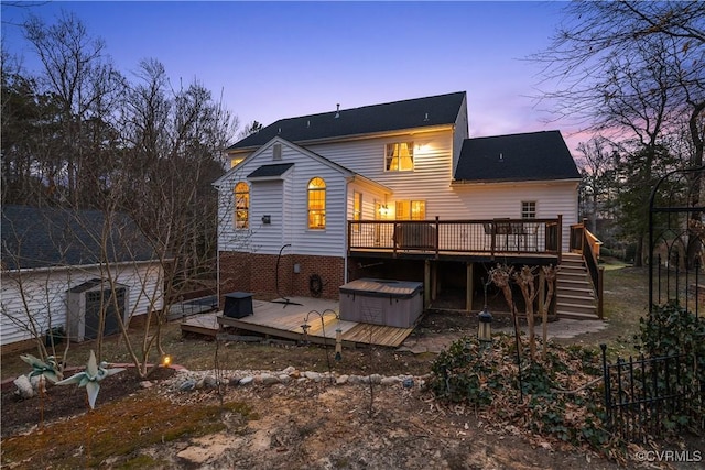 back of house at dusk with stairway, a hot tub, fence, and a deck