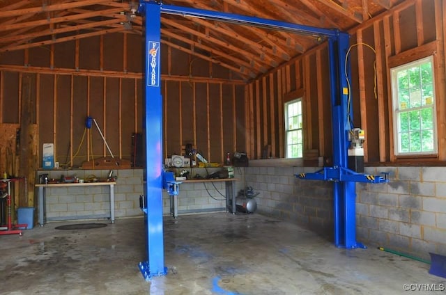 misc room featuring lofted ceiling, concrete floors, concrete block wall, and a workshop area