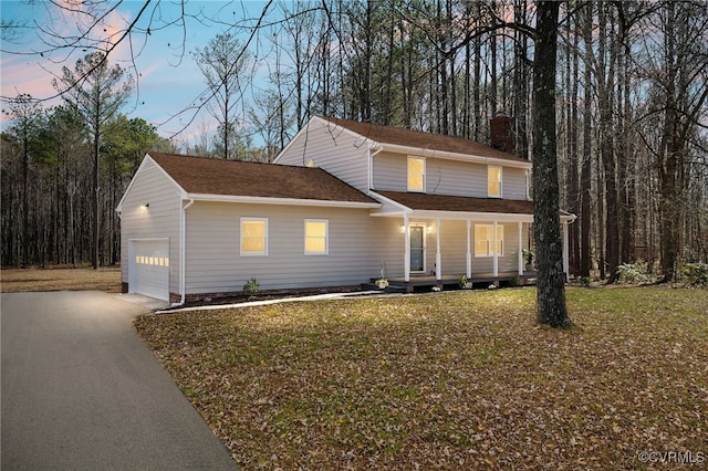 traditional-style house with a garage, driveway, covered porch, and a front yard