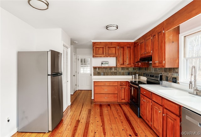 kitchen featuring light wood finished floors, a sink, stainless steel appliances, light countertops, and under cabinet range hood