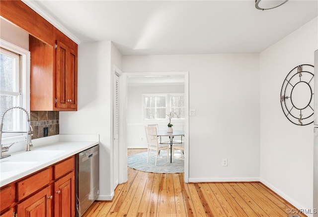 kitchen featuring light wood finished floors, a sink, stainless steel dishwasher, light countertops, and decorative backsplash