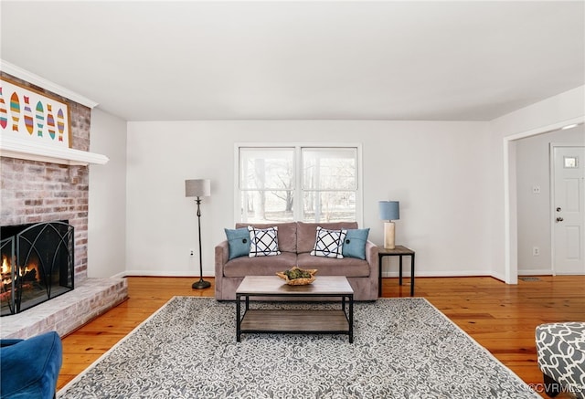 living room featuring a brick fireplace, baseboards, and wood finished floors