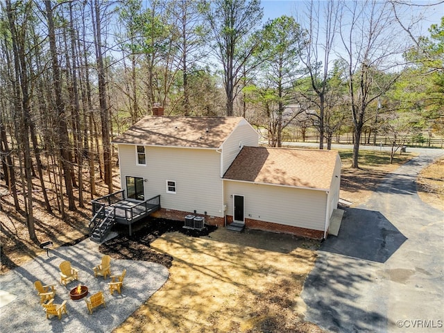 exterior space featuring a deck, central AC unit, a shingled roof, and a fire pit