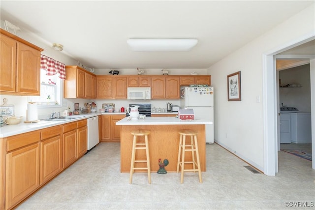 kitchen with a breakfast bar, visible vents, a sink, white appliances, and independent washer and dryer