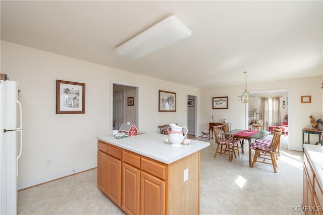 kitchen with baseboards, a center island, hanging light fixtures, freestanding refrigerator, and light countertops