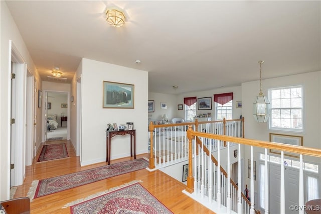 corridor featuring an inviting chandelier, baseboards, wood finished floors, and an upstairs landing