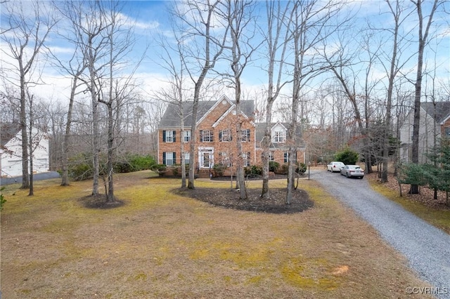 view of front facade featuring gravel driveway, a front yard, and brick siding