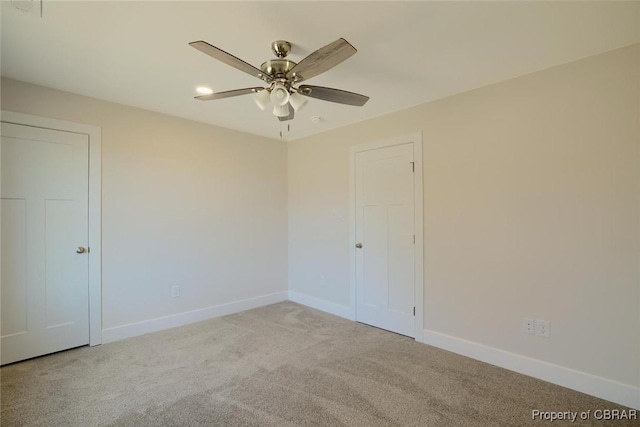 carpeted spare room featuring ceiling fan and baseboards