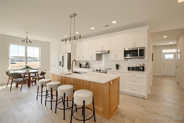 kitchen featuring a center island with sink, appliances with stainless steel finishes, a kitchen breakfast bar, a sink, and backsplash