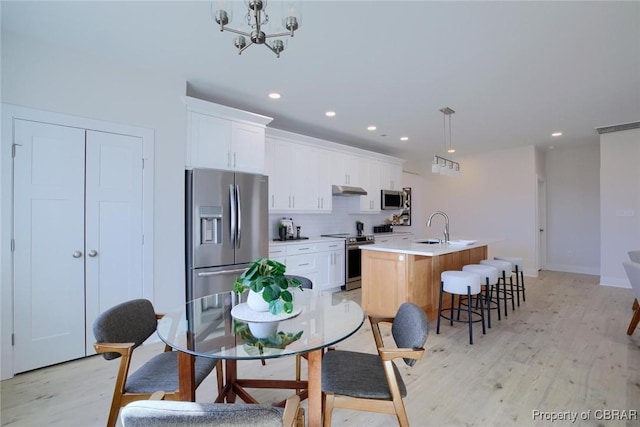 kitchen with appliances with stainless steel finishes, a sink, an island with sink, light wood-type flooring, and under cabinet range hood