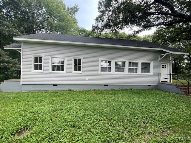 back of house featuring crawl space, roof with shingles, and a yard