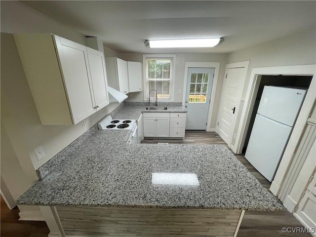 kitchen featuring light stone counters, a peninsula, white appliances, a sink, and white cabinetry