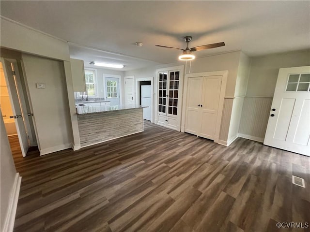 unfurnished living room featuring a ceiling fan, baseboards, visible vents, and dark wood-type flooring