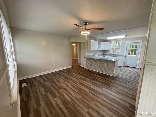 kitchen with a peninsula, a sink, baseboards, white cabinets, and dark wood finished floors