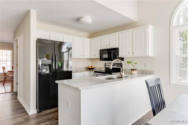 kitchen featuring light stone counters, a peninsula, black appliances, white cabinetry, and a sink