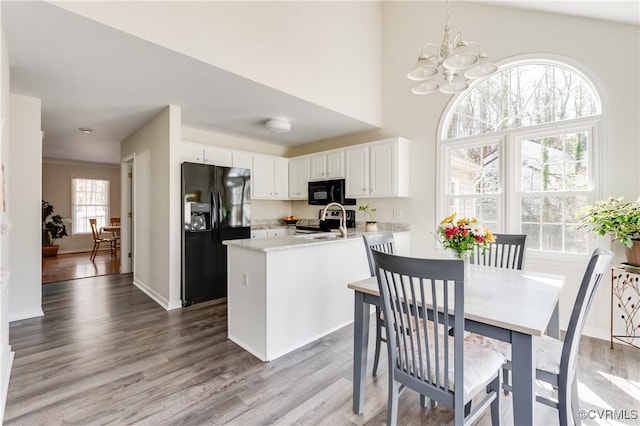 kitchen featuring a peninsula, wood finished floors, white cabinets, light countertops, and black appliances