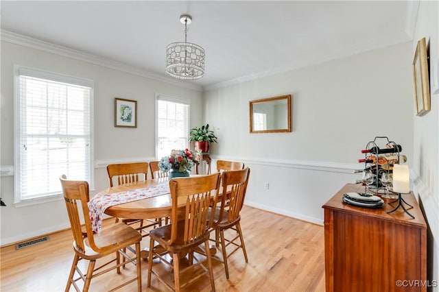 dining area featuring light wood finished floors, ornamental molding, a chandelier, and visible vents