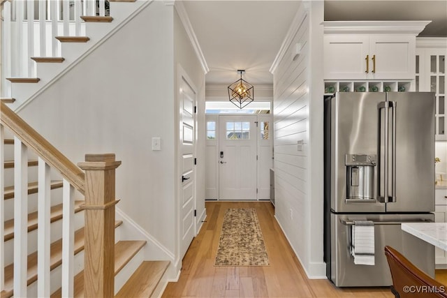 entryway with ornamental molding, stairway, and light wood-style floors