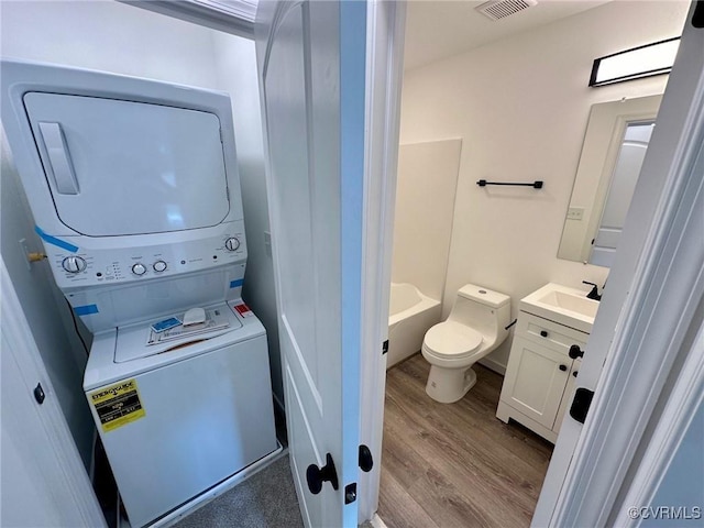 full bathroom with stacked washer / drying machine, visible vents, toilet, vanity, and wood finished floors