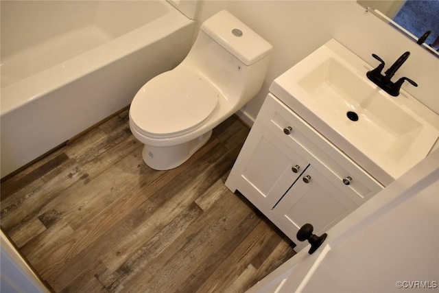 bathroom with toilet, a tub, wood finished floors, and vanity