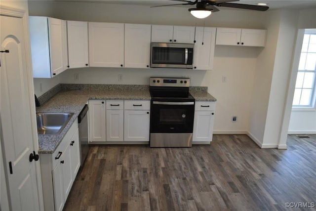 kitchen with a sink, white cabinetry, baseboards, appliances with stainless steel finishes, and dark wood finished floors