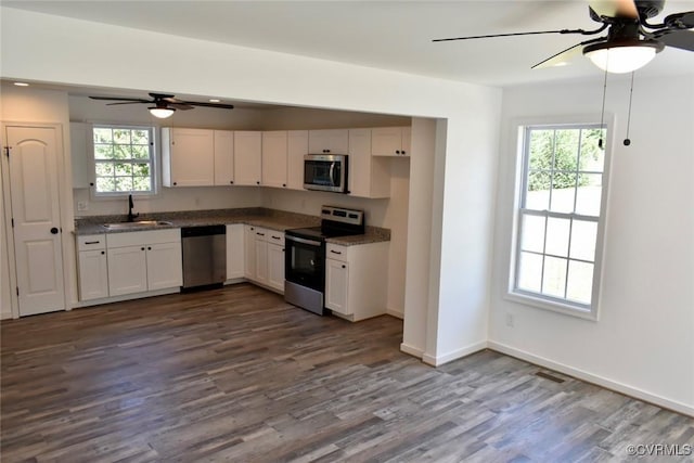 kitchen featuring dark wood-style floors, stainless steel appliances, dark countertops, white cabinets, and a sink