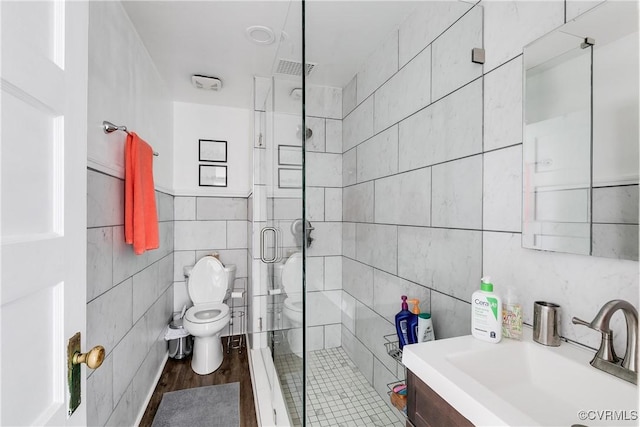 bathroom featuring toilet, a stall shower, tile walls, and vanity