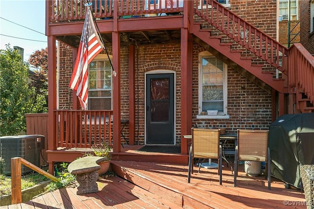 entrance to property with a deck, brick siding, and central air condition unit