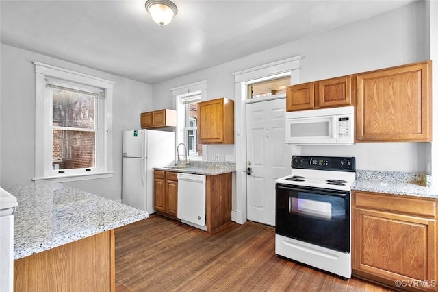 kitchen featuring dark wood-style floors, light stone counters, brown cabinets, a sink, and white appliances