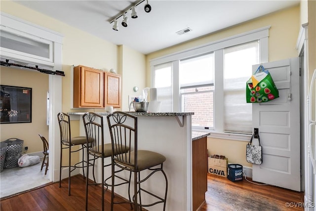 kitchen featuring visible vents, a kitchen breakfast bar, dark stone countertops, dark wood-style flooring, and a peninsula