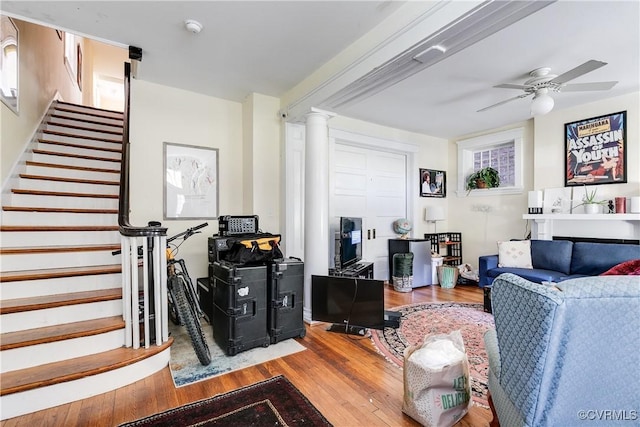 living area featuring ornate columns, stairs, a ceiling fan, and wood finished floors