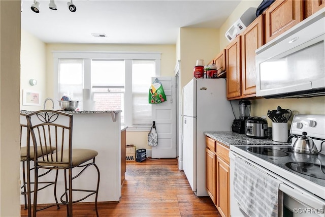 kitchen featuring white appliances, visible vents, brown cabinets, light wood finished floors, and a kitchen bar