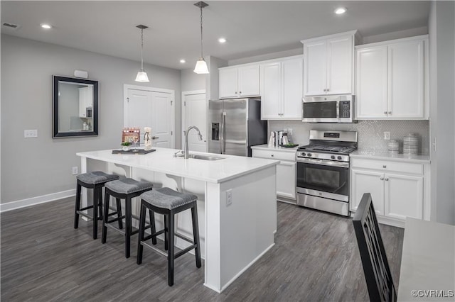 kitchen featuring an island with sink, dark wood-type flooring, a sink, stainless steel appliances, and backsplash