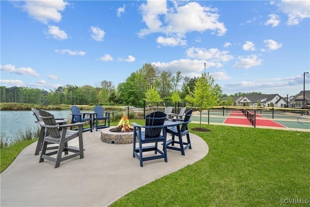 view of community featuring a fire pit, a tennis court, a water view, fence, and a yard