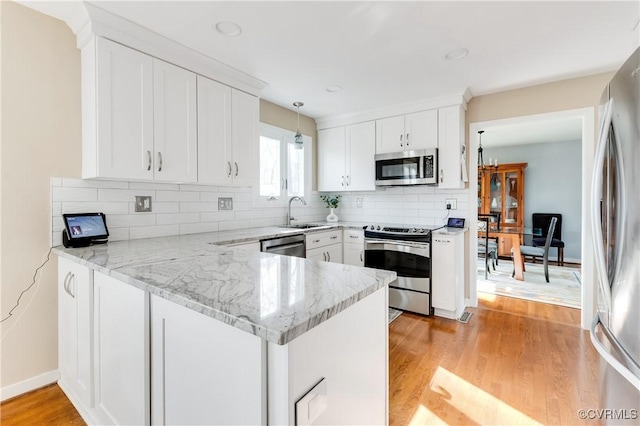 kitchen with tasteful backsplash, light wood finished floors, a peninsula, white cabinets, and stainless steel appliances