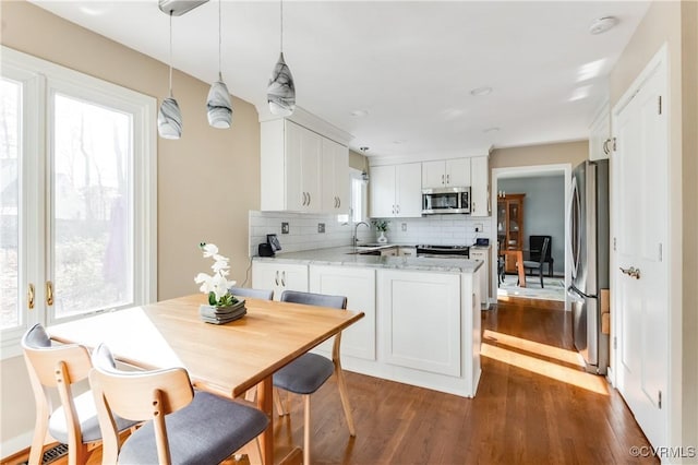 kitchen featuring wood finished floors, a peninsula, white cabinets, appliances with stainless steel finishes, and tasteful backsplash