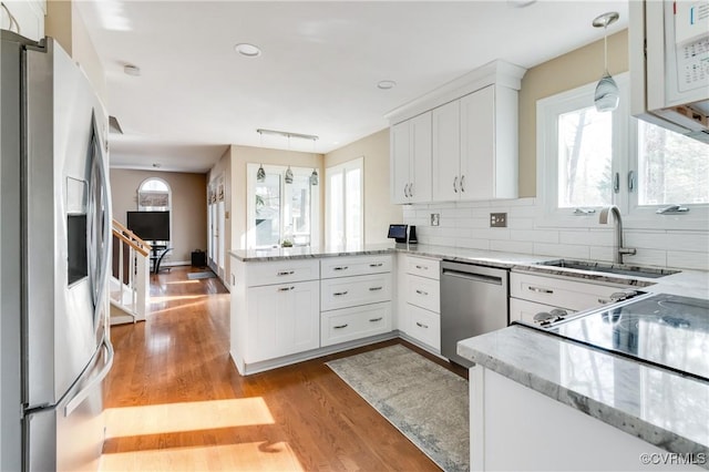 kitchen featuring a sink, stainless steel appliances, light wood-style floors, a peninsula, and white cabinets