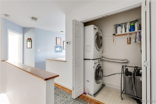 laundry room featuring laundry area, light floors, stacked washer and clothes dryer, and baseboards