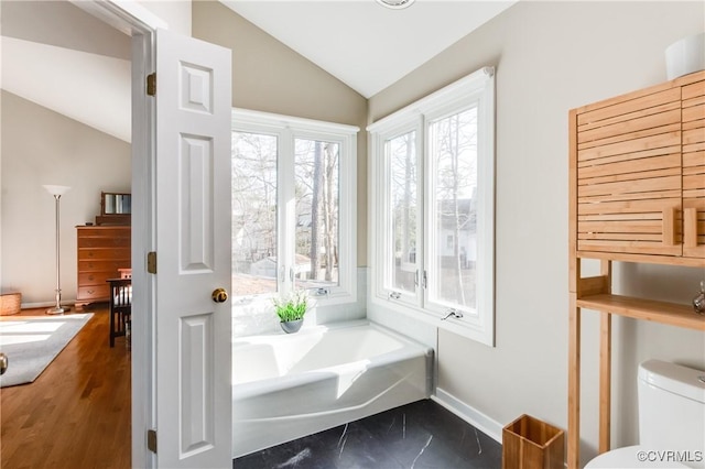 bathroom featuring toilet, marble finish floor, baseboards, a bath, and vaulted ceiling