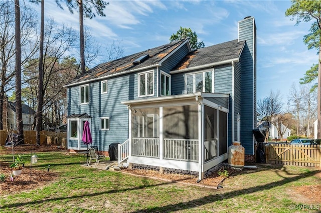 rear view of property featuring a chimney, a sunroom, a yard, and fence