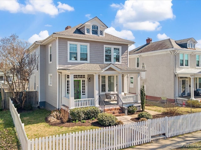 american foursquare style home with a fenced front yard, a chimney, a porch, and roof with shingles