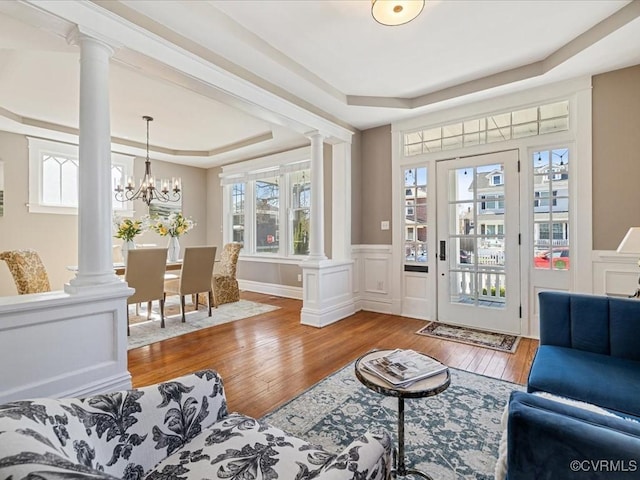 interior space featuring a raised ceiling, wainscoting, hardwood / wood-style flooring, ornate columns, and a decorative wall