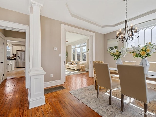 dining room with a tray ceiling, hardwood / wood-style flooring, decorative columns, and an inviting chandelier