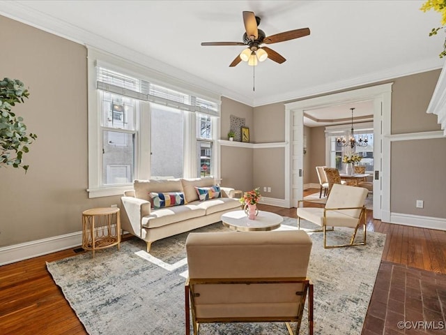 living area with ornamental molding, wood-type flooring, baseboards, and ceiling fan with notable chandelier